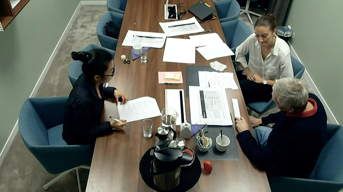 Four people around a meeting table covered with printed sketches and notes.